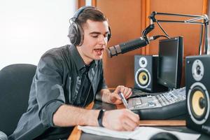 Talks and uses mic. Young man is indoors in the radio studio is busy by broadcast photo