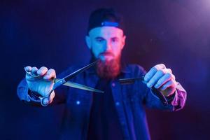 Young bearded barber in cap standing in the studio with neon lighting photo
