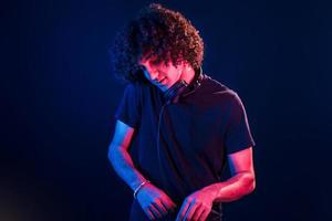 Young DJ with curly hair standing in the club with neon light photo