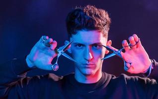 Holds scissors. Young barber with work equipment standing in the studio with neon lighting photo