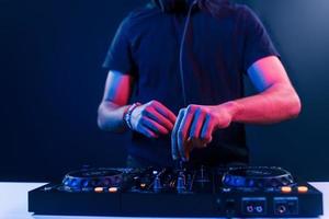 Close up view of DJ's hands that working with music equipment in the club with neon lighting photo