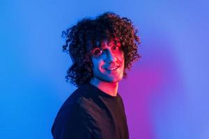 un joven hermoso con el pelo rizado está en el interior del estudio con luces de neón foto