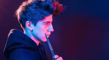 Holds scissors. Young barber with work equipment standing in the studio with neon lighting photo