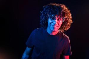 Young beautiful man with curly hair is indoors in the studio with neon lighting photo