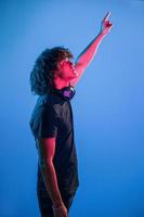 With headphones. Young beautiful man with curly hair is indoors in the studio with neon lighting photo