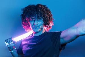 Holds lighting equipment. Young beautiful man with curly hair is indoors in the studio with neon lighting photo