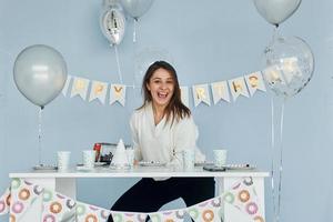 Young woman in formal clothes sits by festive table and smiling. Concept of birthday holiday photo