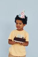 Happy little african american kid have fun indoors at birthday party holds cake photo