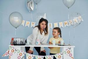 Una joven divertida se divierte preparando una mesa de cumpleaños con una niña foto