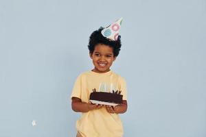 Happy little african american kid have fun indoors at birthday party holds cake photo