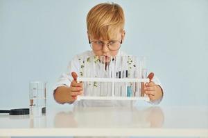Uses test tubes. Little boy in coat playing a scientist in lab by using equipment photo