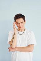 Young gay man is standing in the studio and posing for a camera. In casual white shirt photo