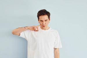 Young gay man is standing in the studio and posing for a camera. In casual white shirt photo