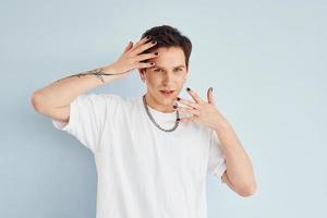 Young gay man is standing in the studio and posing for a camera. In casual white shirt photo