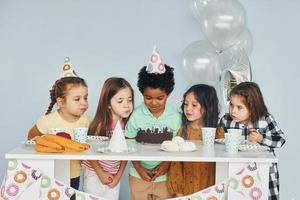 se sienta junto a la mesa. los niños que celebran la fiesta de cumpleaños en el interior se divierten juntos foto