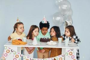 Sits by the table. Children on celebrating birthday party indoors have fun together photo