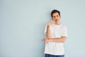 Young gay man is standing in the studio and posing for a camera. In casual white shirt photo