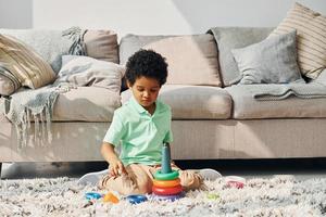 niño afroamericano juega con juguetes en el interior cerca de la cama en casa foto