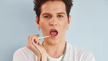 Young gay man is standing in the studio and posing for a camera. Paints lips with lipstick photo