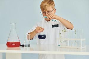 Little boy in coat playing a scientist in lab by using equipment photo