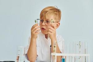 Uses test tubes. Little boy in coat playing a scientist in lab by using equipment photo