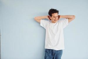 Young gay man is standing in the studio and posing for a camera. In casual white shirt photo