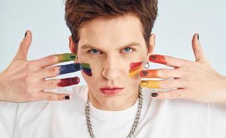 joven gay está parado en el estudio y posando para una cámara. pintado por maquillaje multicolor foto