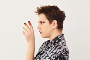 Young gay man is standing in the studio and posing for a camera. Multicolored make up on face fingers photo