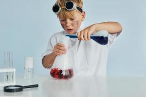 Little boy in coat playing a scientist in lab by using equipment photo