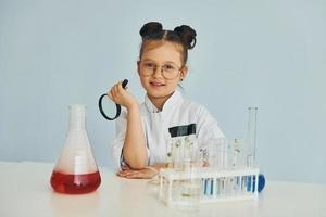 Works with test tubes. Little girl in coat playing a scientist in lab by using equipment photo