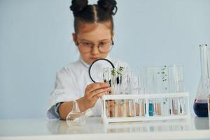 Holds magnifying glass. Little girl in coat playing a scientist in lab by using equipment photo