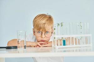 Uses test tubes. Little boy in coat playing a scientist in lab by using equipment photo