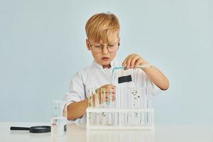 Little boy in coat playing a scientist in lab by using equipment photo