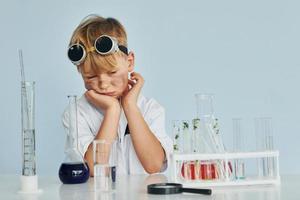 Scared little boy in coat playing a scientist in lab by using equipment photo