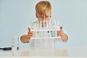 Uses test tubes. Little boy in coat playing a scientist in lab by using equipment photo