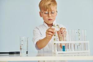 Uses test tubes. Little boy in coat playing a scientist in lab by using equipment photo