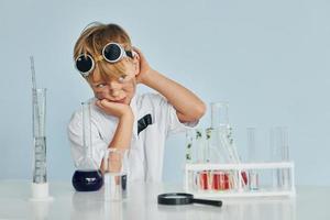 Scared little boy in coat playing a scientist in lab by using equipment photo