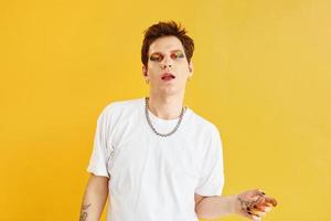 Young gay man is standing in the studio and posing for a camera. Against yellow background photo