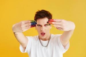 Young gay man is standing in the studio and posing for a camera. Rainbow make up photo