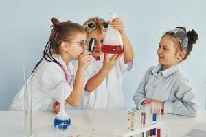 Standing by the table with test tubes. Children in white coats plays a scientists in lab by using equipment photo