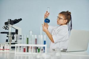 Little girl in coat playing a scientist in lab by using equipment photo