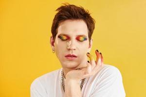 joven gay está parado en el estudio y posando para una cámara. maquillaje de arcoiris foto