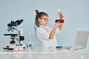 Little girl in coat playing a scientist in lab by using equipment photo