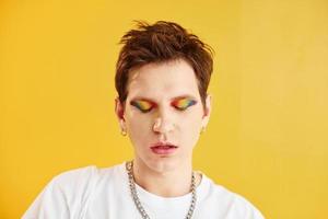 Young gay man is standing in the studio and posing for a camera. Against yellow background photo