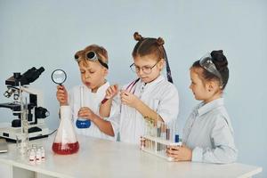 los niños con batas blancas juegan a los científicos en el laboratorio usando equipos foto