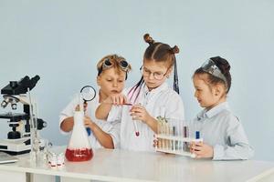 los niños con batas blancas juegan a los científicos en el laboratorio usando equipos foto