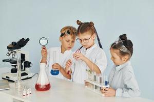 los niños con batas blancas juegan a los científicos en el laboratorio usando equipos foto