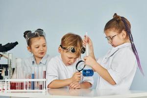 los niños con batas blancas juegan a los científicos en el laboratorio usando equipos foto