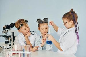 los niños con batas blancas juegan a los científicos en el laboratorio usando equipos foto