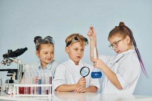 los niños con batas blancas juegan a los científicos en el laboratorio usando equipos foto